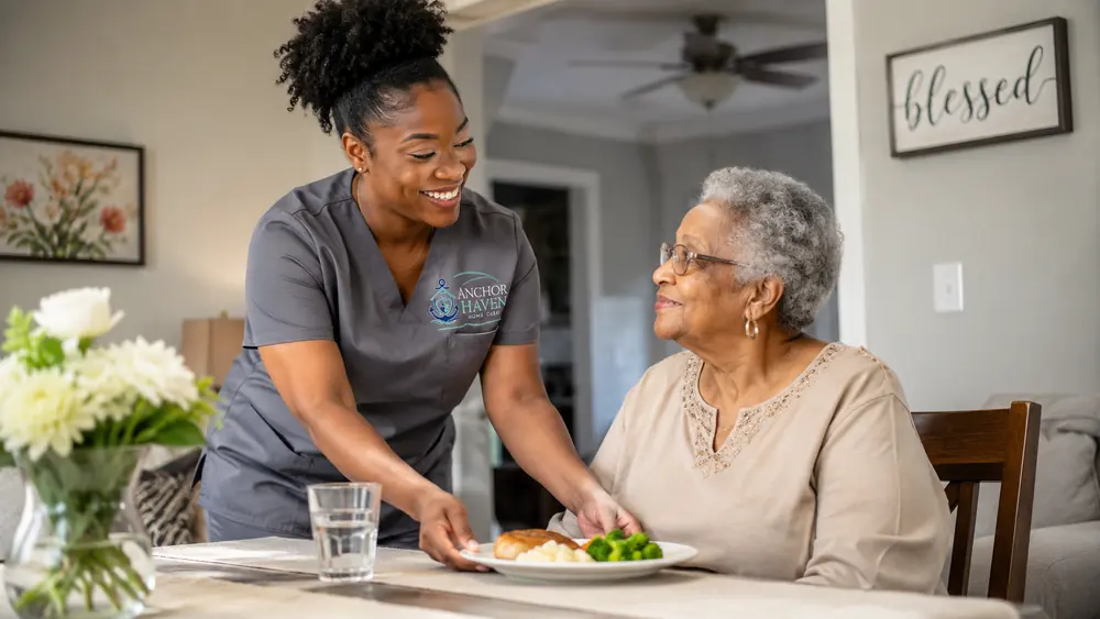 A caregiver setting down a plated hot meal in front of a seated older woman.